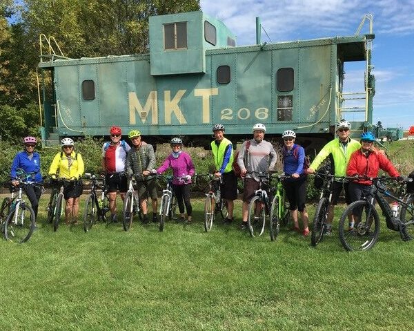 Self-guided riders posing in front of a green MKT train car.