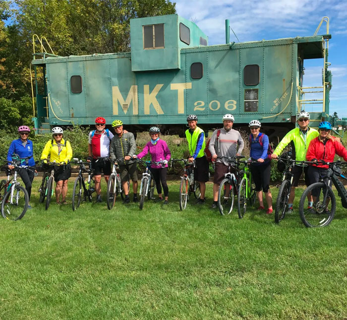 A large group of bikers in front of an MKT railroad train car.